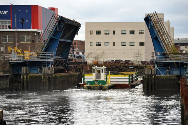 After a barge is filled with dredged materials, it is pushed down the Gowanus Canal, past the Third Street Bridge. The Department of Transportation has stationed crews of bridge workers along the canal, to raise and lower bridges throughout the day.